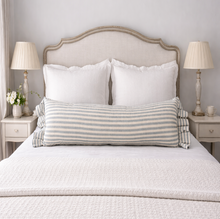 Load image into Gallery viewer, Neatly made bed with striped  long blue and off-white bolster pillow and two lamps on nightstands.