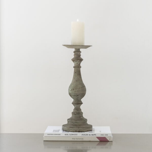 Decorative candlestick with a candle on top of two books against a plain background