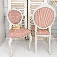 Load image into Gallery viewer, Two pink vintage chairs with greige frames in front of white shutters.